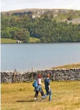  ??  ?? Walkers take in the dramatic beauty of the tarn with the boathouse in the shadow of the trees sheltered by the cliffs opposite.