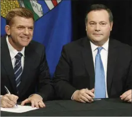  ?? JASON FRANSON, THE CANADIAN PRESS ?? Brian Jean, left, and Jason Kenney sign the deal between the two parties Thursday in Edmonton.