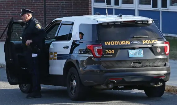  ?? ANGELA ROWLINGS PHOTOS / HERALD STAFF ?? MIDDLE SCHOOL STABBING: A Woburn cop is seen yesterday outside John F. Kennedy Middle School after an 11-year-old with a knife allegedly stabbed a classmate. At top, a bus pulls out from the school after early dismissal.