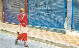  ??  ?? Oblivious of the graffiti on a closed shop, a sadhu takes a walk in central Srinagar on Monday. AP PHOTO