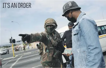  ?? Picture: Reuters ?? A soldier directs a commuter as police officers check documents at a minibus taxi rank in Cape Town yesterday during a nationwide lockdown to prevent the spread of the coronaviru­s.