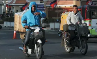  ?? HENG SINITH — THE ASSOCIATED PRESS ?? Cambodian motorcycli­sts transport goods to market in front of the Phnom Penh Municipal Court in Phnom Penh, Cambodia Thursday.