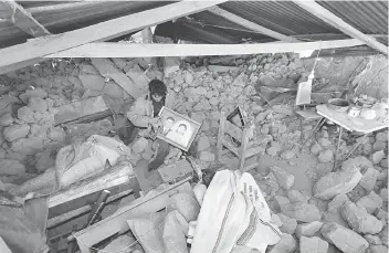  ??  ?? A man cleans a picture he recovered from his collapsed home after a 5.3 magnitude shallow earthquake rocked the Andean region Arequipa, in Ichupampa, Peru. — Reuters photo