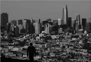  ?? AP Photo/Jeff Chiu ?? In this 2020 file photo, a person wearing a protective mask walks in front of the skyline on Bernal Heights Hill during the coronaviru­s pandemic in San Francisco.