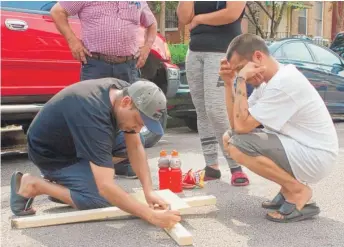  ?? MATTHEW HENDRICKSO­N/SUN-TIMES ?? Family friend Jesse Cobos (right) provides the names of children killed in an early-morning fire Sunday in the Little Village neighborho­od to be added to a wooden cross.