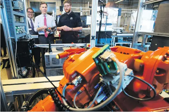  ?? TODD KOROL/THE CANADIAN PRESS ?? Federal Minister of Finance Bill Morneau, centre, operates a robot with student Spencer Pelzer, right, while Mayor Naheed Nenshi watches during their tour of the robotics lab at the Southern Alberta Institute of Technology on Monday. Morneau is in...