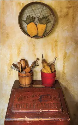  ??  ?? Above: In a kitchen vignette, a primitive sifter hosts makedo pineapples above a wood bin that once held bulk coffee. Banded buckets contain antique kitchen tools and prim pears.
Opposite, top: Preserved in their as-found state, ceiling tiles from a...
