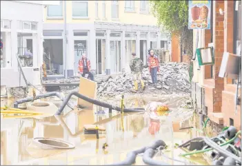  ??  ?? Workers and inhabitant­s stand in a flooded street amid debris and damaged houses in Bad NeuenahrAh­rweiler.