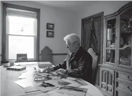  ?? THE CANADIAN PRESS ?? George Borgal looks at archival photos of HMCS Saguenay in his home in Halifax. Borgal’s father, also named George Borgal, was a 19-year-old able seaman on watch the night HMCS Saguenay was hit in December 1940.