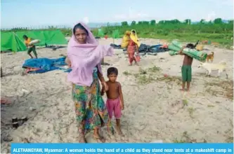  ??  ?? ALETHANGYA­W, Myanmar: A woman holds the hand of a child as they stand near tents at a makeshift camp in Rakhine state in Myanmar, while waiting to find a way to cross over into Bangladesh. — AFP