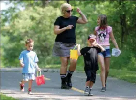  ?? JONATHAN TRESSLER — THE NEWS-HERALD ?? Northeast Ohio mom Holly Heron, center, holds up a rock she painted to resemble a watermelon slice as she and her children, from left, 4-year-old Gavin, 5-year-old Nolan and 11-year-old Bela Moore, seek hiding spots at a city park for the other painted...