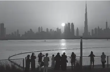  ?? Associated Press ?? People watch the sunset over the skyline, with Burj Khalifa at right, in Dubai, United Arab Emirates. The film "Geostorm" marks just the latest movie in which Western filmmakers put the commercial capital of the United Arab Emirates in its crosshairs....