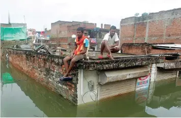  ?? — Reuters ?? Men sit on the roof of a partially submerged shop in a flooded residentia­l colony in Allahabad.