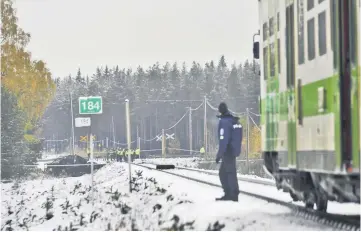  ??  ?? Rescue and military personnel and a policeman stand at the railroad crossing at the site of a crash between a train and a military truck near Raseborg. — AFP photo