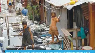  ??  ?? PHNOM PENH: Cambodian children wade in polluted water at a village in Phnom Penh.