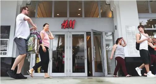  ??  ?? People walk past a H&M clothing store in Miami Beach, Florida. H&M has apologized for a controvers­ial advert in Britain that showed a black child model wearing a hooded sweatshirt that said “coolest monkey in the jungle.” (Getty Images)