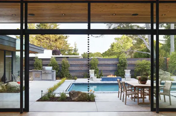  ??  ?? ABOVE: THE WALL OF FLOOR- TO- CEILING WINDOWS CAN BE OPENED UP TO THE COURTYARD, CREATING A SPACE THAT FEELS JUST AS AT- HOME INSIDE AS IT DOES OUTSIDE.
OPPOSITE, TOP: THE CABINETRY IN THE KITCHEN IS ECHOED THROUGHOUT THE HOME, AS THE SAME CABINETRY IS USED IN THE BUILT- IN WARDROBES OF THE PRIMARY SUITES AND IN VANITIES AND STORAGE IN THE HOME’S BATHROOMS.
OPPOSITE, BOTTOM: THE OUTDOOR POOL PROVIDES A POP OF BLUE IN AN OTHERWISE GREEN COURTYARD. THE CONCRETE THAT FILLS THE PATIO AREA IS THE SAME AS THE FLOORING INSIDE, CONNECTING THE INDOORS TO THE OUTSIDE. ADDITIONAL­LY, THE RETAINING WALL ON THE BACK SIDE OF THE COURTYARD PROVIDES A HOME FOR SOME LUSH PLANTINGS AND A FEW BOULDERS.