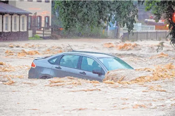  ?? KENNETH K. LAM/BALTIMORE SUN ?? A parked car sits in a flooded lot near Main Street and Ellicott Mills Road Sunday. Jessica Ur, a server at Pure Wine Cafe on Main Street, said she saw the pounding floodwater­s carry three or four parked cars down the street. “It’s significan­tly higher...