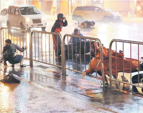  ??  ?? Motorcycli­sts fall as Typhoon Nesat hits Taipei. — Reuters photo