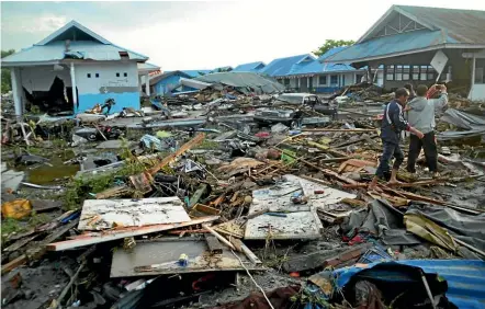  ??  ?? Men survey the damage following earthquake­s and a tsunami in Palu, Central Sulawesi, Indonesia.AP