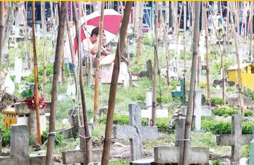  ?? SUNSTAR FOTO / ALEX BADAYOS ?? THEY’RE NOT CROSS WITH EACH OTHER. Two visitors to the cemetery in Pardo, Cebu City share an umbrella while chatting in the middle of some graves.