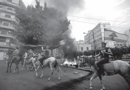  ?? Ibrahim CHALHOUB / AFP ?? LEBANESE protesters ride horses past burning tires in front of the house of former sports minister Faisal Karami, during a protest against dire economic conditions in the coastal city of Tripoli to the north of Beirut, Lebanon on October 18, 2019.