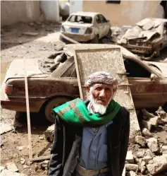  ??  ?? A man stands next to cars damaged by an air strike in Amran, Yemen. — Reuters photo