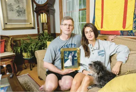  ?? CLOE POISSON/SPECIAL TO THE COURANT ?? Kirk Murad and daughter Murphy sit in the living room of their Storrs home on Friday with their dog and a photo of Kirk with his wife, Pattie Wu-murad, on their wedding day 33 years ago. Wu-murad went missing in April while on a pilgrimage hiking through the mountains of Japan.