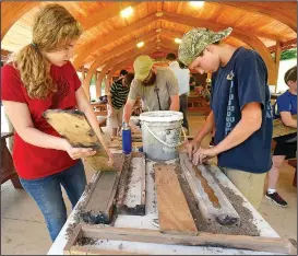  ?? NWA Democrat-Gazette/FLIP PUTTHOFF ?? Avery Batson (left) smooths sand Friday while Jackson Ellington (right) places his wooden sword in his box of sand to create a mold for a metal sword.