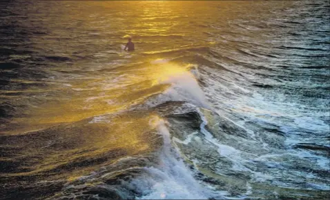  ?? Jonah Markowitz / The New York Times ?? A surfer in a wetsuit waits as winds whip the surf at Rockaway Beach in New York on Dec.. At least seven young people drowned last year along Rockaway Beach.