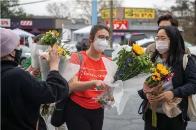  ?? The Associated Press ?? Roula AbiSamra, center, and Chelsey (last name withheld), right, prepare Wednesday to lay flowers bouquets at a makeshift memorial outside of the Gold Spa in Atlanta. Police in the Atlanta suburb of Gwinnett County say they’ve begun extra patrols in and around Asian businesses there following the shooting at three massage parlors in the area that killed eight, most of them women of Asian descent.