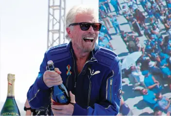  ?? (Joe Skipper/Reuters) ?? RICHARD BRANSON prepares to spray champagne after flying with a crew in Virgin Galactic’s passenger rocket plane ‘VSS Unity’ on July 11.