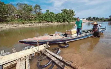  ?? BERNAMA PIC ?? Din Mamat (right) pushing his boat to the riverbank of Sungai Golok in Pasir Mas.