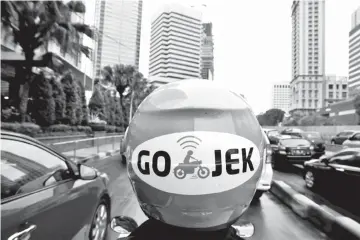  ?? — Reuters pic ?? A Go-jek driver rides his motorcycle through a business district street in Jakarta.