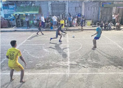  ??  ?? People play football on a street in Yangon.
