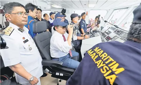  ??  ?? Abang Johari uses binoculars to look at the sea onboard KM Sri Aman yesterday.