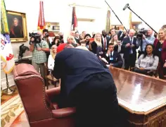  ?? — Reuters/WP-Bloomberg photos ?? West bends down and hugs President Trump behind his desk during a meeting in the Oval Office of the White House in Washington, on Thursday. (Far left) West shows Trump a photo of an airplane during the meeting.