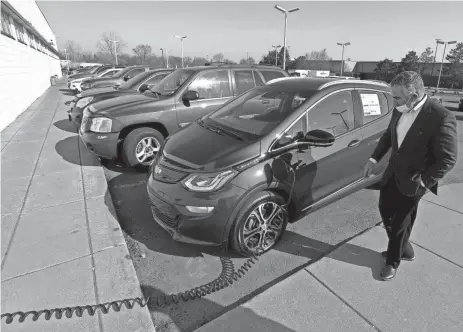  ?? ERIC SEALS/DETROIT FREE PRESS ?? Ralph Shaheen, president of Shaheen Cadillac and Chevrolet in Lansing, looks over a Chevy Bolt EV parked and getting a charge. Next door at his Cadillac dealership, Shaheen had it fitted to prepare for new EV models.