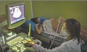  ??  ?? Mendoza receives a fetal ultrasound showing her unborn daughter who she will name Peyton, from her obstetrici­an at a private medical clinic where visits average $20 in Caracas, Venezuela. Her partner, Leo Camejo, began selling hamburgers from home, earning enough to pay for the prenatal care appointmen­ts.