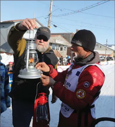  ?? Photo by Diana Haecker ?? IT’S A WRAP— Jason Mackey of Knik was the last Iditarod musher off the trail on Friday, March 17 at 5:03 p.m. after a trail time of 12 days, two hours and three minutes. He extinguish­ed the widow’s lantern, held by Iditarod Race Marshal Mark Nordman.