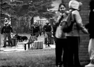  ?? PETER POWER/TORONTO STAR ?? Students huddle in the rain after being let out of lockdown yesterday at Chinguacou­sy Secondary School while Peel police officers wrap up a search after a shooting.