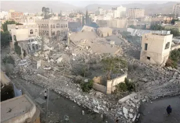  ??  ?? File photo shows people walking past a building one day after air strikes destroyed it in Sanaa, Yemen.