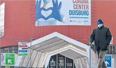  ?? MARTIN MEISSNER/AP ?? A man passes a musical theater, which has been turned into a COVID-19 test and vaccinatio­n center, Jan. 25 in Duisburg, Germany.