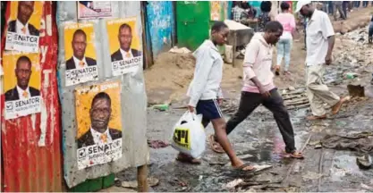  ??  ?? NAIROBI: Kenyans walk past election posters in the Kibera slum. — AFP