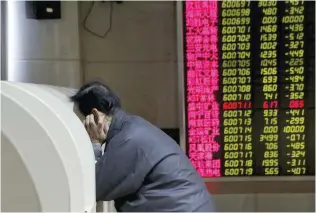  ?? — Reuters ?? An investor uses a monitor to check stock informatio­n on desk in front of an electronic board showing stock informatio­n in Beijing, China.