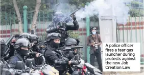  ??  ?? A police officer fires a tear gas launcher during protests against the new Job Creation Law