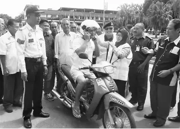  ??  ?? Nurlila putting a helmet on the first motorcycli­st passing by while Gabriel (on Nurlila’s right) and others look on.