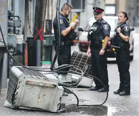  ?? DAN JANISSE ?? Police officers inspect the carnage after two large air-conditioni­ng units were ripped from their rooftop perches and tossed into an alley three storeys below. Police arrested a suspect they believe may have been trying to access copper he could sell for cash to buy drugs.