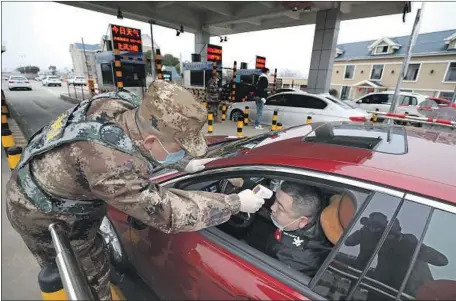  ?? Chinatopix ?? A DRIVER’S TEMPERATUR­E is taken at a highway checkpoint Thursday in Wuhan, China, a city of 11 million where the coronaviru­s appears to have originated. Experts see President Xi Jinping’s responses as a sign of progress since the SARS outbreak of 2002 and 2003.