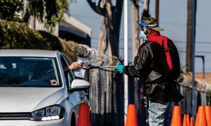  ?? Photograph: Apu Gomes/AFP/Getty Images ?? A testing center worker uses a stick to collect tests at a drive through site in Los Angeles.